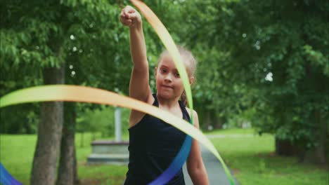 a young girl skillfully manipulating colorful ribbons in a lush green park, showcasing her artistic expression and focus during outdoor physical activity