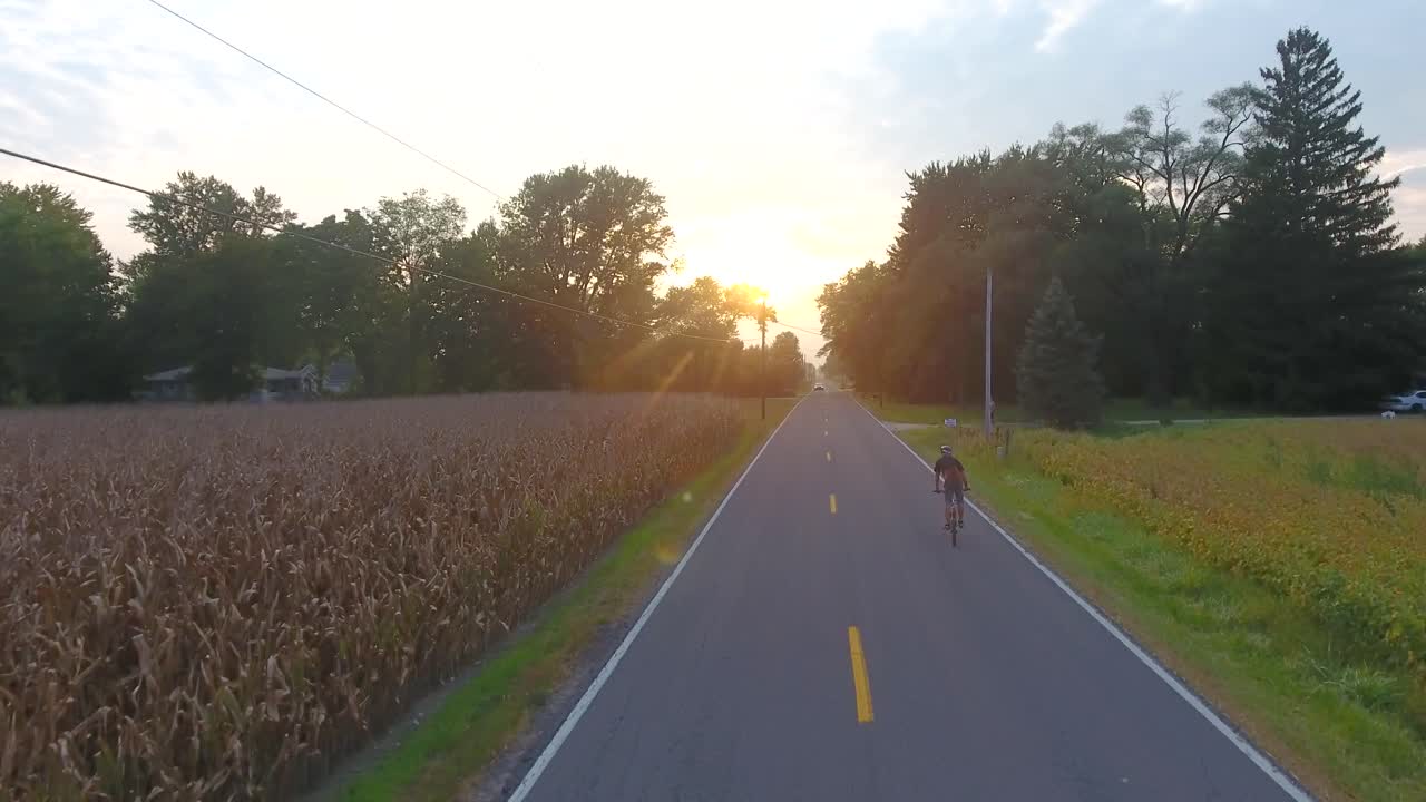 Aerial view of young man on bike ride in country down a road during sunset in 4K