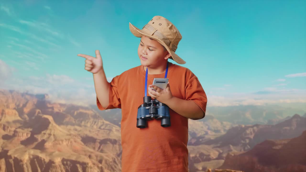 Asian Boy With A Hat And Binoculars Looking At Smartphone Then Smiling And Pointing To Side While Traveling At The Top Of Mountain. Boy Researcher Examines Something, Travel Tourism Adventure Concept