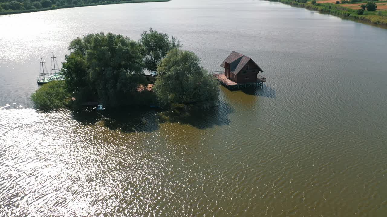 Small island and a house in the middle of the river. Aerial view of beautiful green island surrounded by water. Camera moves round.