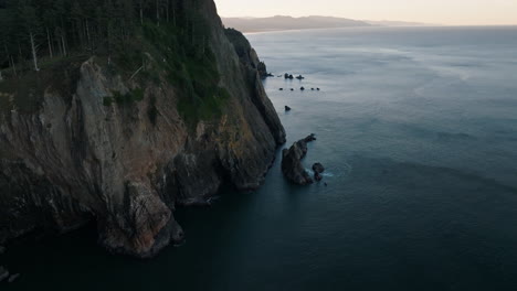 drone pushes forward past dry dirt cliff as grass drops off into ocean along the oregon coast