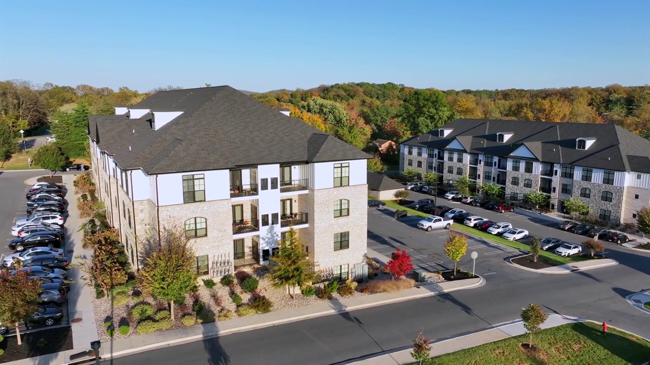 Luftoptagelse, der nærmer sig et nyt moderne lejlighedshus om efteråret. Blå himmel med farverige træer i et forstadskvarter. Parkerede biler på parkeringspladsen. Amerikansk kvarter med luksusbygninger.