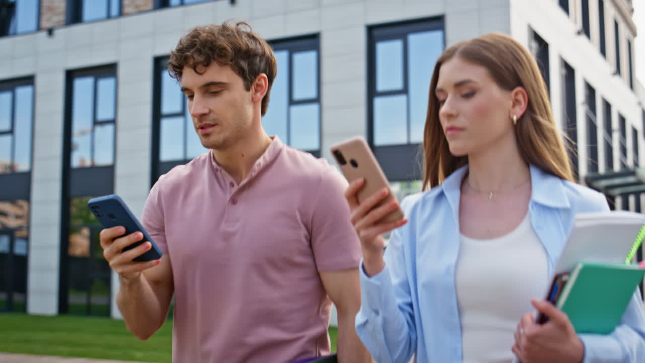 Walking managers using smartphones outdoors by modern urban building closeup