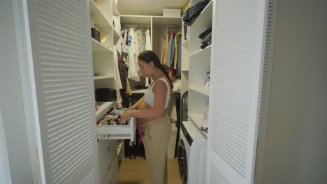 a pregnant woman standing in a modern walk-in closet, thoughtfully selecting an outfit. the scene features stylish clothing and a serene, cozy atmosphere