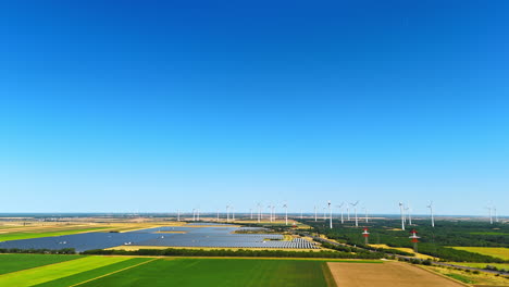 approaching the modern sites of solar fields installed in the countryside. wind farms work at backdrop. aerial view