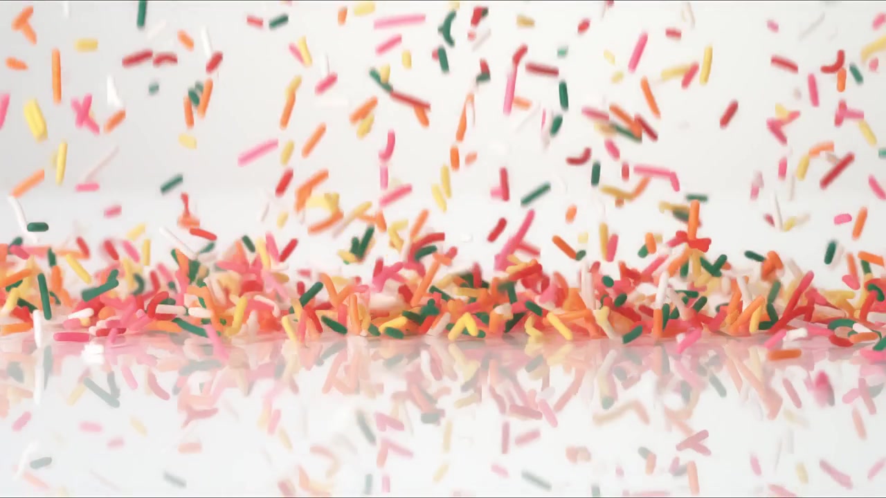 Birthday party celebration Rainbow Sprinkles bouncing on a white tabletop in slow motion close up macro before settling.
