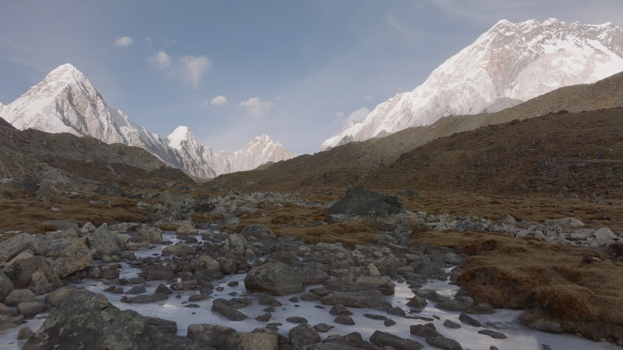 tomada aérea de bajo ángulo de un río congelado en lobuche en la caminata del campamento base del everest, nepal, con las montañas everest y pumori en el fondo