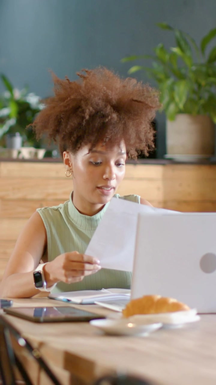 Vertical video: Flipping pages woman in mint top reading docs for work at cafe pc peer placing cup