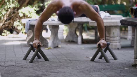 man performing push-ups on parallettes in a park