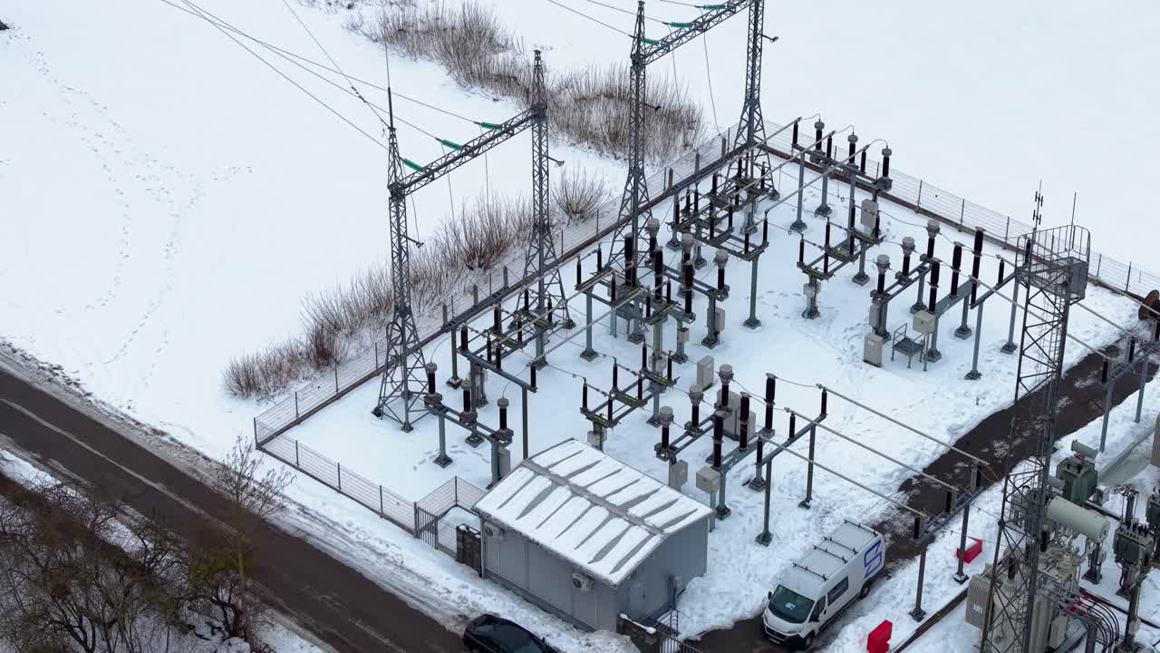 Drone video capturing a snow-dusted electrical substation set amidst a serene winter landscape. The industrial structures contrast beautifully against the white backdrop