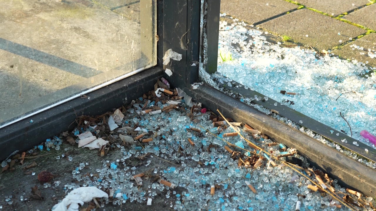 Vetri rotti e mozziconi di sigaretta in una pensilina di fermata dell'autobus sporca e vandalizzata