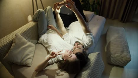 Cheerful-beautiful-young-couple-selfie-on-sofa-home-using-polaroid-camera