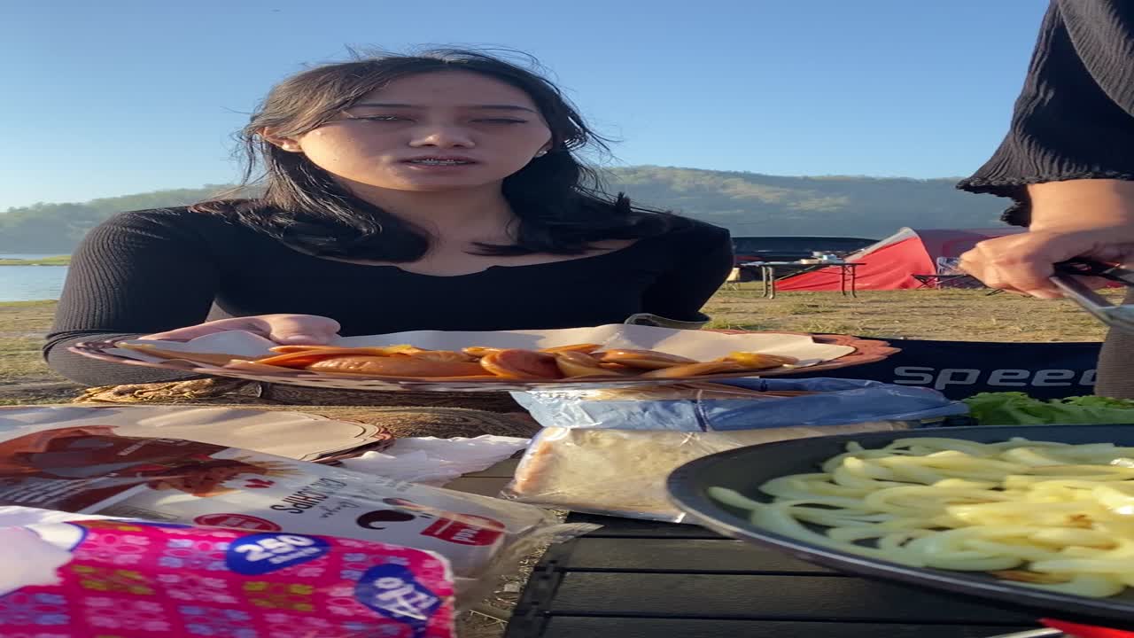 vertical footage, with friends camping and making breakfast of bread, sandwiches, sausages with a view of the clean Sermo reservoir.