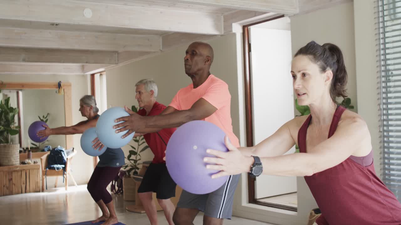 Anziani diversi che fanno esercizi tenendo delle palle con un'allenatrice di Pilates, al rallentatore