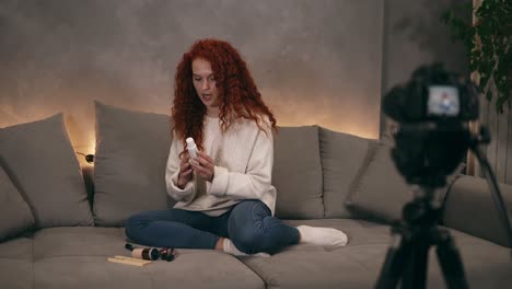 Curly-redhead-young-girl-vlogger-is-talking-in-front-of-camera-recording-video-for-online-blog-in-internet,-demosrating