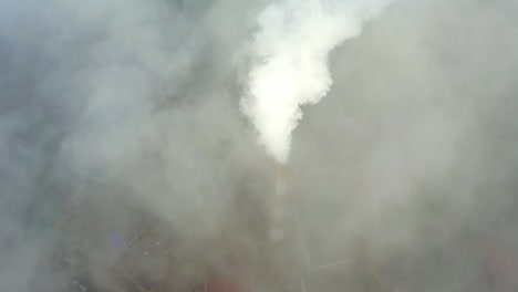 smoke from a power station chimney rising from a low, creeping fog. drone view