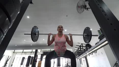 footage of a pregnant female model doing squats in a gym trying to keep fit in her fourth trimester