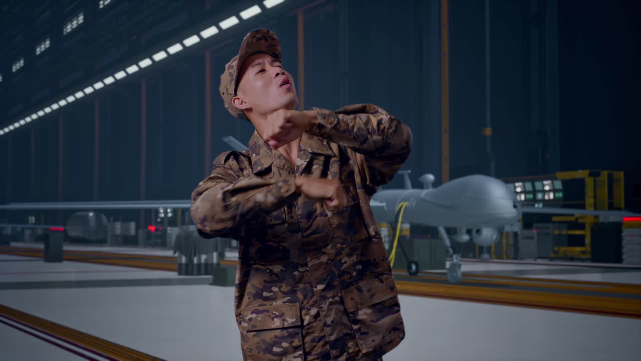 Soldato asiatico che balla mentre è in piedi con un moderno drone militare in un hangar di manutenzione.