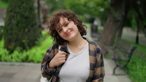 retrato de una chica morena feliz en una camisa a cuadros caminando por el parque y posando durante un descanso entre clases en la universidad