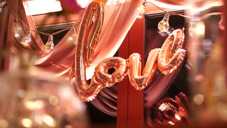 the word "love" made of pink balloons, with a backdrop of a light bulb garland