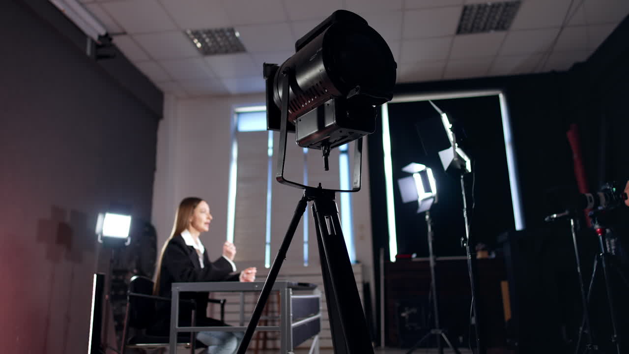 Soffit on tripod in studio. Low angle view. Female at desk talks to camera in the lights of soffits at backdrop.