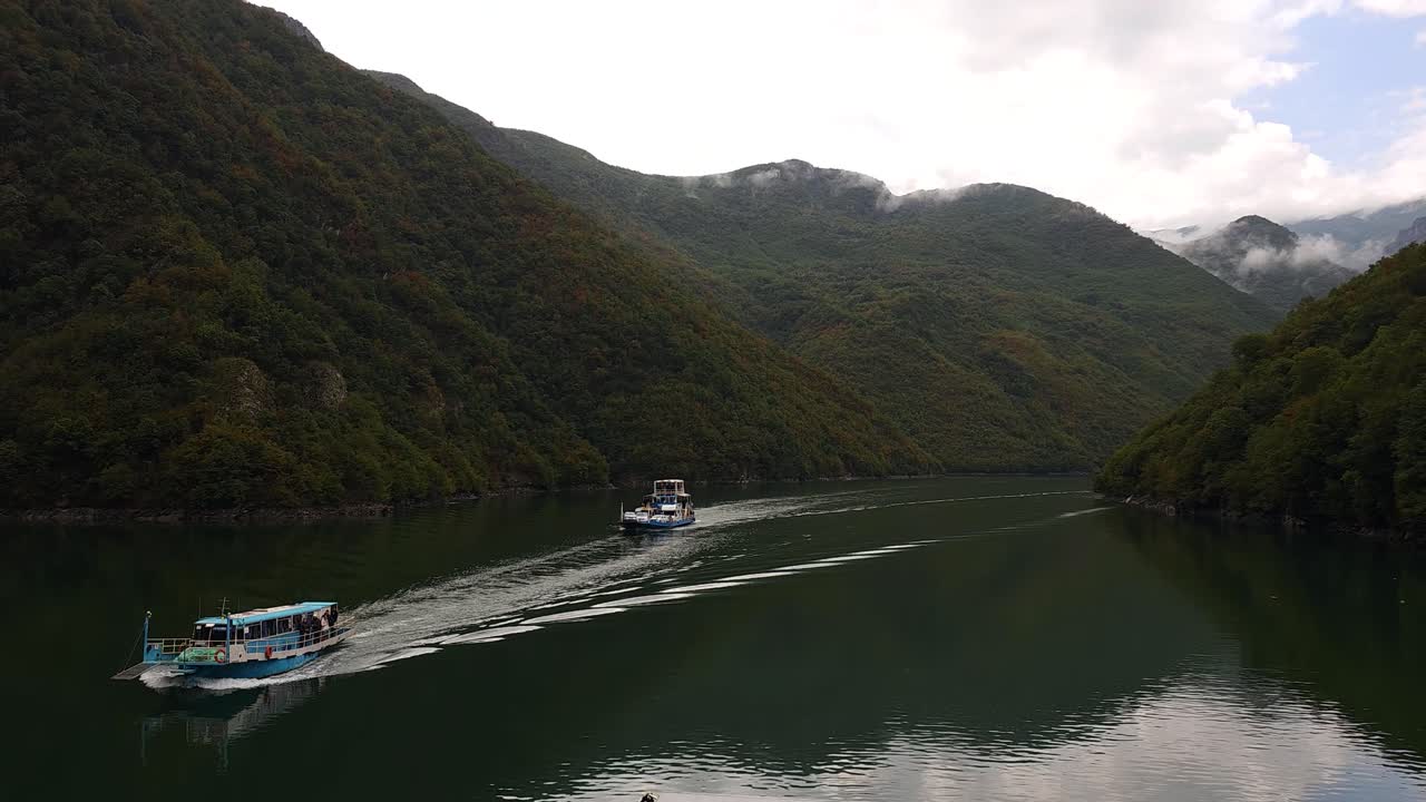 알파인 바다의 평온함: 알바니아의 코만 산 호수의 조용한 아름다움 속에서 항해하는 배, 구름이 가득한 날 계곡
