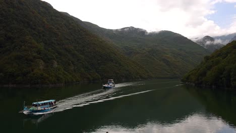 serenidad en las aguas alpinas: barcos navegando en medio de la belleza tranquila del lago de montaña koman en albania, valle de día nublado