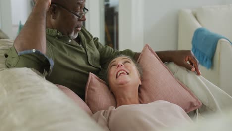 Happy-senior-diverse-couple-wearing-shirts-and-watching-tv-in-living-room