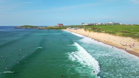 Surfistas-De-La-Playa-Fistral-Cabalgando-Las-Olas-Del-Océano-Con-Vistas-Al-Hotel-Headland-Y-Al-Campo-De-Golf,-Newquay,-Reino-Unido