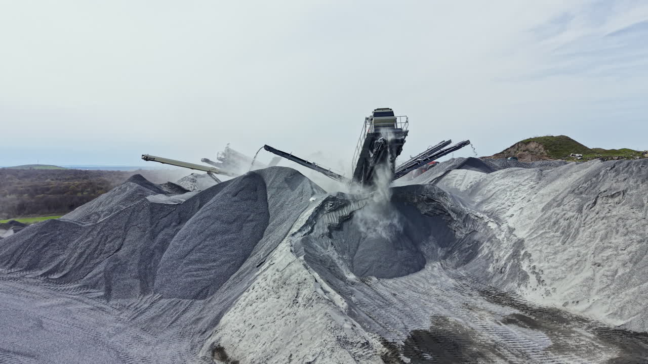 Activity in a granite quarry with machinery processing rock materials and creating dust clouds in a work environment