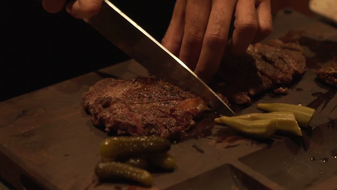 Slow motion static shot of grilled wagyu beef steak being sliced on a cutting board in HD 1080p 23.98p