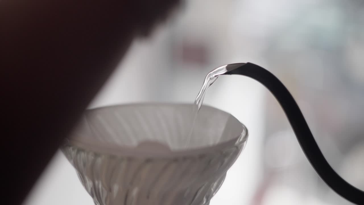 Close up of a gooseneck kettle pouring hot water in V60 coffee dripper with steam and clear water.