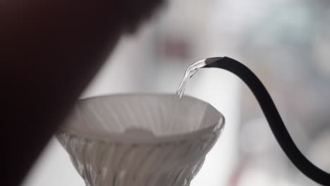 close up of a gooseneck kettle pouring hot water in v60 coffee dripper with steam and clear water.