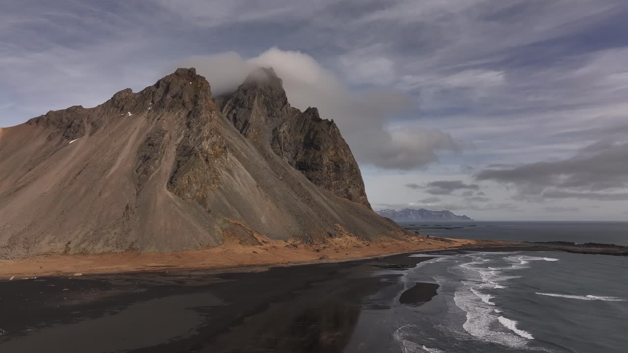 ocean waves touch black shore beneath towering Vestrahorn cliffs in Iceland