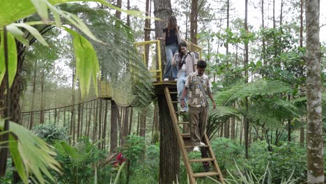 indonesian friends descending treehouse ladder in forest during nature adventure