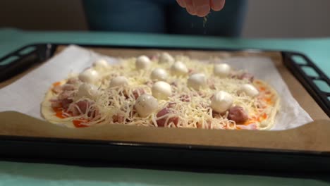 mano poniendo suavemente orégano en pizza casera