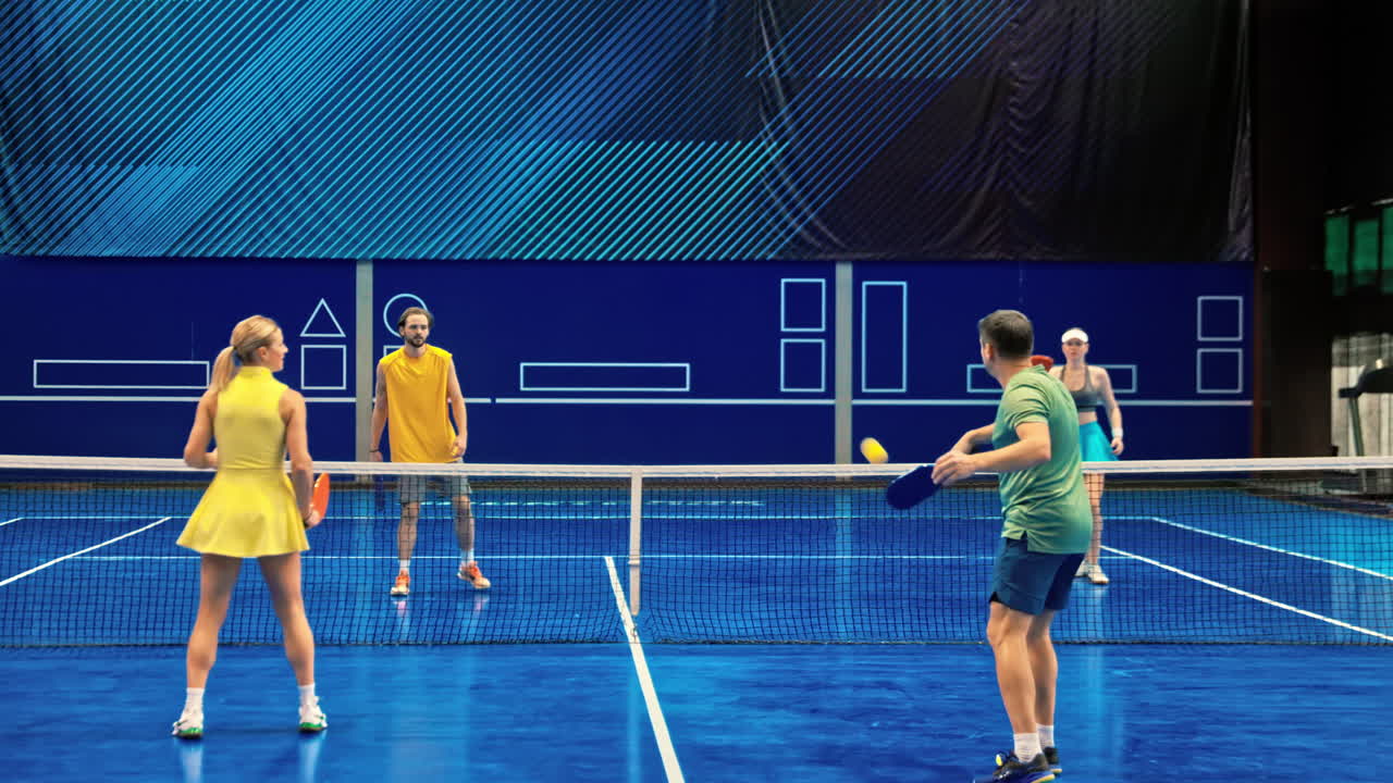 Two men and two women playing pickleball on a blue, inside court