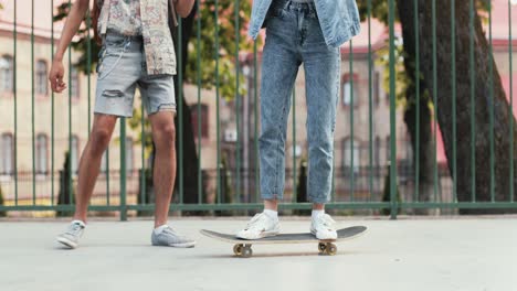 vista completa de una adolescente montando una patineta mientras su novio afroamericano la ayuda a mantener el equilibrio en la calle