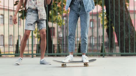 vista de corpo inteiro de uma adolescente andando de skate enquanto seu namorado afro-americano a ajuda a manter o equilíbrio na rua