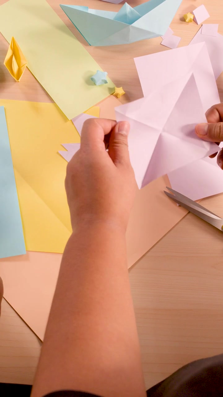 Mani che piegano e tagliano carta colorata per origami su un piano di lavoro ben illuminato