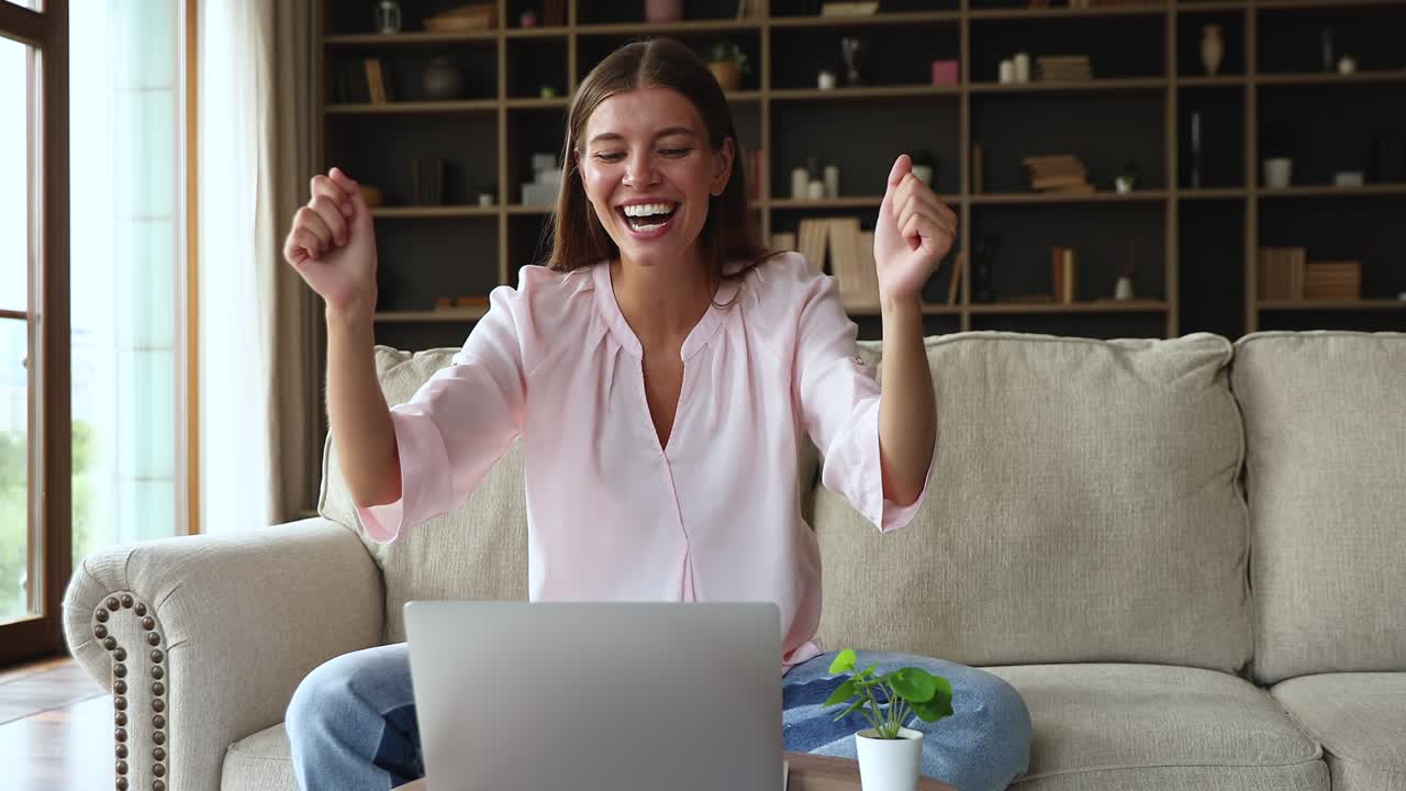 mujer millennial emocionada sentada junto a una computadora portátil ganando un premio en línea