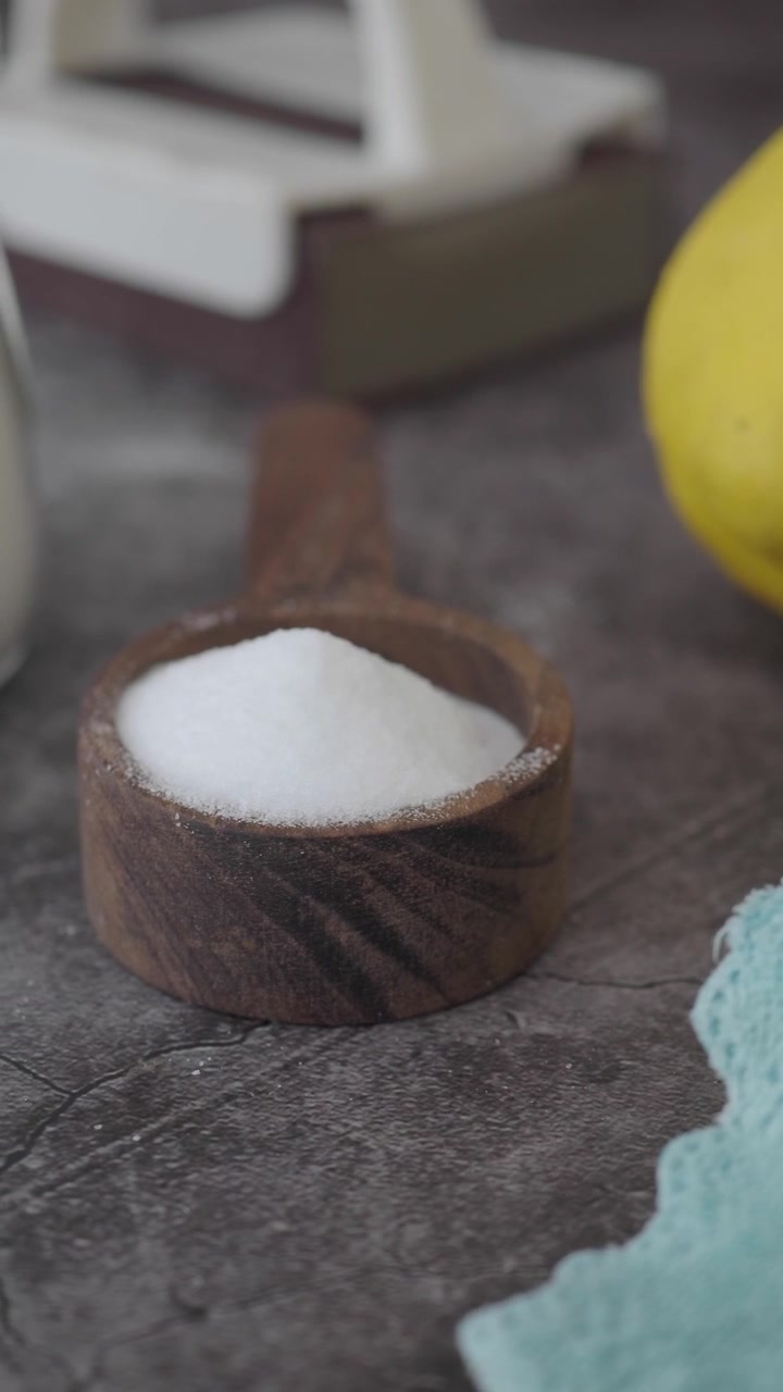 Zucchero bianco in un cucchiaio di legno su una superficie strutturata.