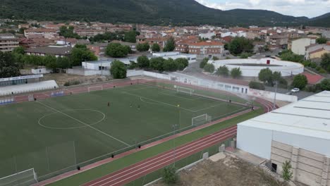 drone flight where we see some sports facilities with a soccer field that are watering the grass with water sprinklers, there are people doing sports