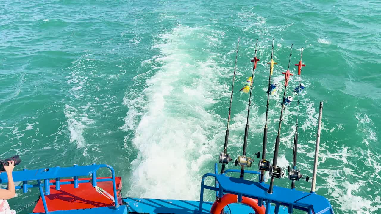 A boat moves through turquoise waters, fishing rods visible, creating a dynamic wake under bright sunlight