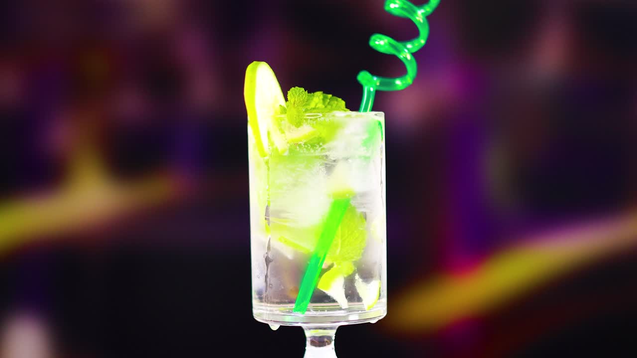 A vibrant mojito cocktail with lime and a green spiral straw, set against a blurred colorful background