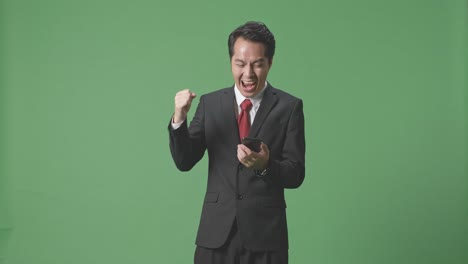 행복 한 아시아 사업가 는 스튜디오 에서 녹색 스크린 에 스마트폰 을 사용 하는 동안 축하