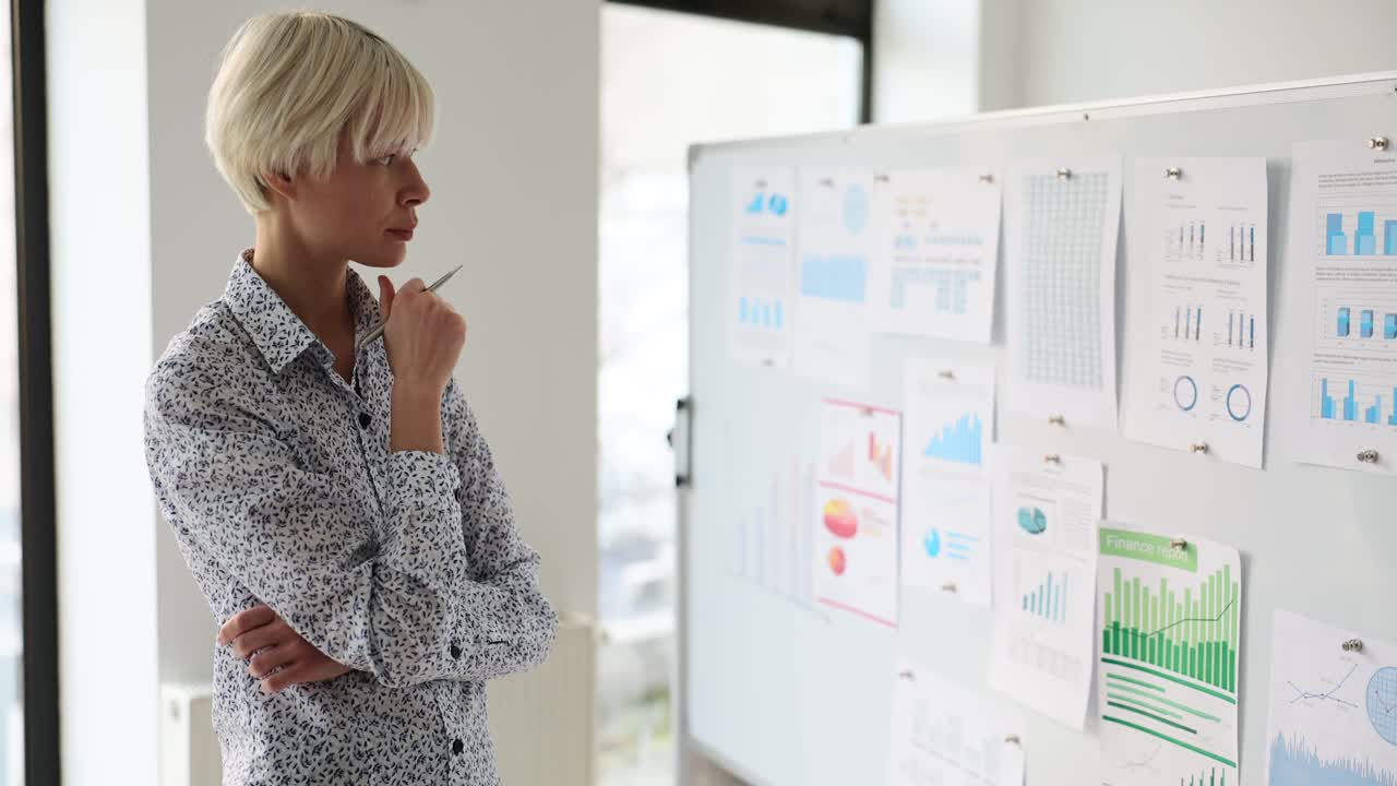 Woman employee thinks looking at diagrams on white board