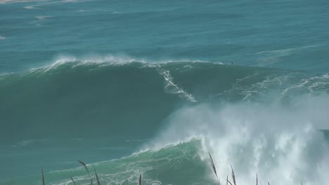 Surfer-riding-giant-wave-near-historical-landmark-Fort-of-Sao-Miguel-Arcanjo-Lighthouse-in-Nazare,-Portugal