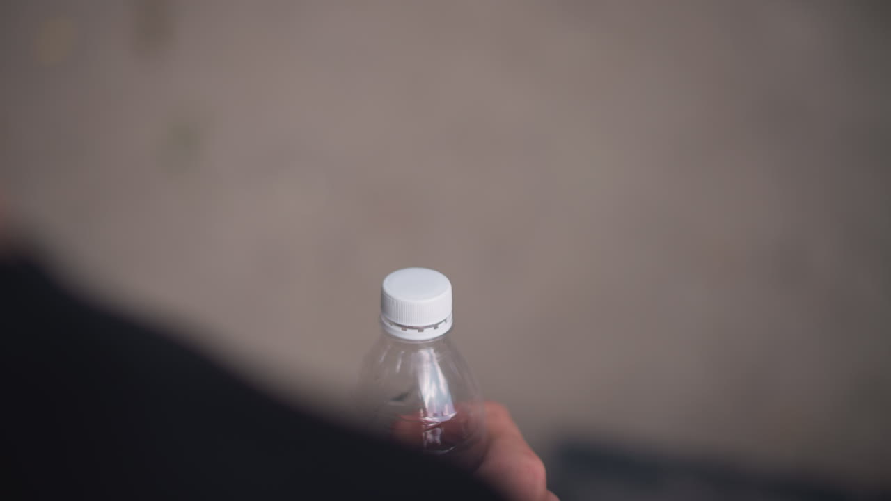 Hands Unscrewing Bottle, Detailed Shot Of Hands Removing Cap, Close View Of Hands Twisting Plastic Bottle Cap Off, Focus On Hands As They Unscrew Water Bottle Cap Amidst City Park Surroundings
