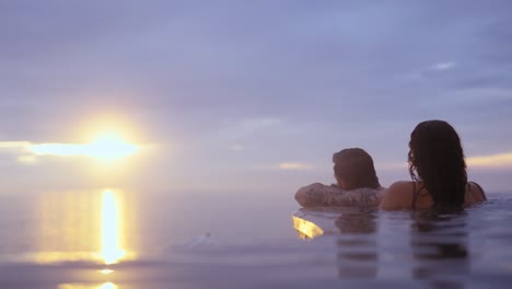 picturesque view of couple relaxing in infinity pool enjoying sunset over ocean